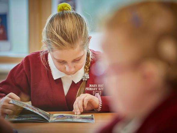 A young student is studiously looking at a book in a classroom