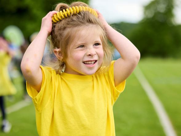 A young pupil is holding a piece of sports equipment above her head on Sports Day.