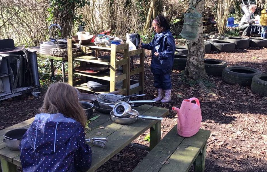 Children are in the woods discovering trees and playing at wooden benches