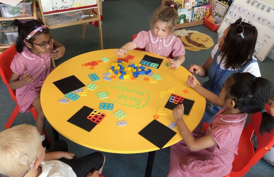 Children are sitting at a table making shapes with coloured pieces