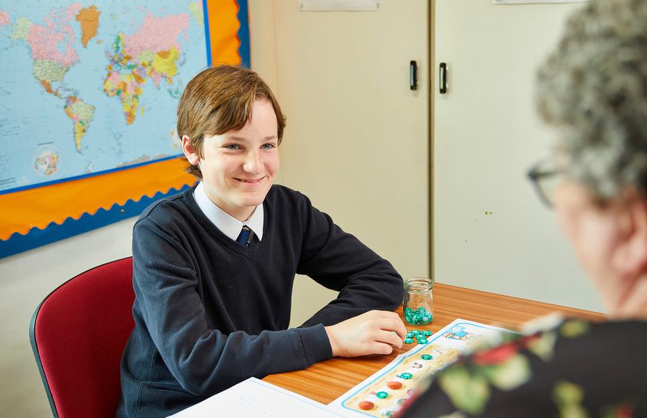 A pupil is sitting at a desk facing a speech therapist