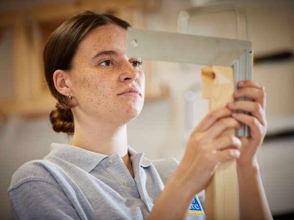 A young female student is measuring wood