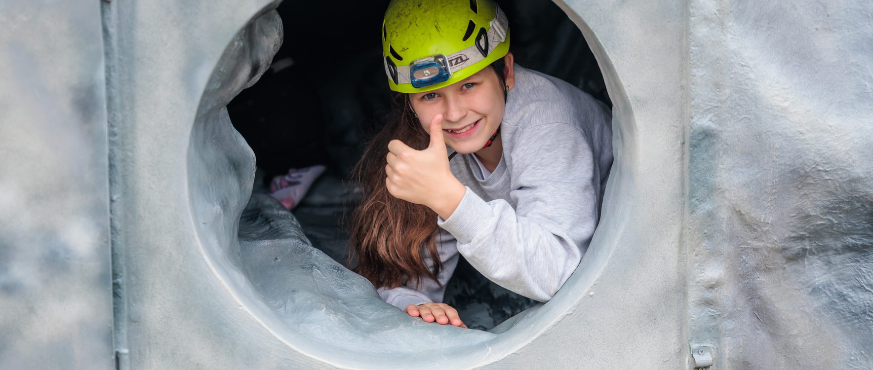 Young girl wearing a bright yellow helmet, whilst taking part in the caving tunnel activity.