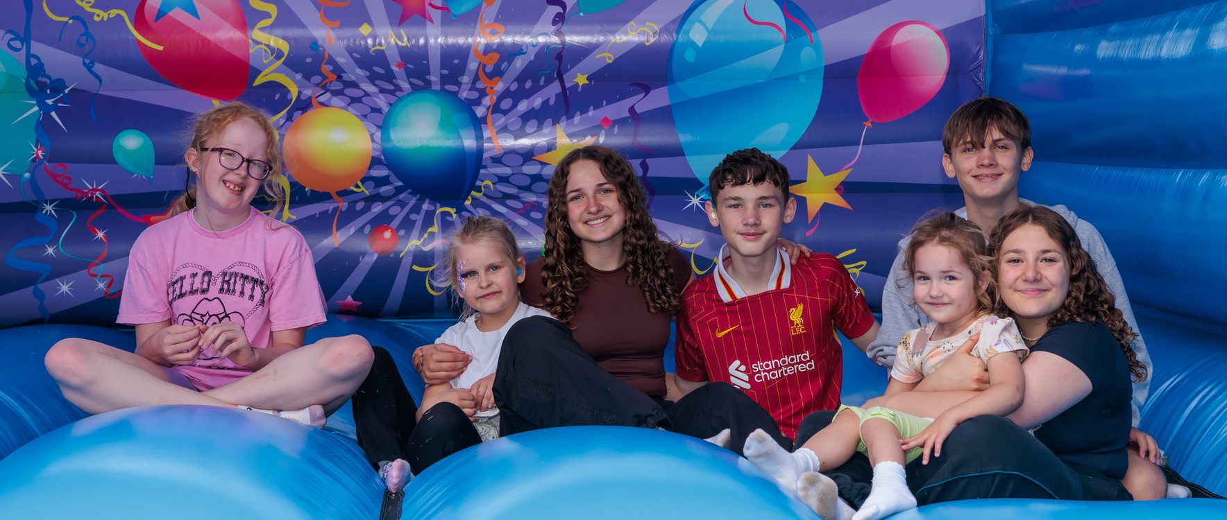 Group Photo of Children sat on a Bouncy Castle smiling.