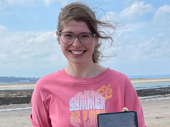 A young female is smiling whilst holding her phone with her results on it.