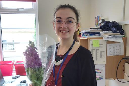 A young female is smiling and holding a bunch of flowers.