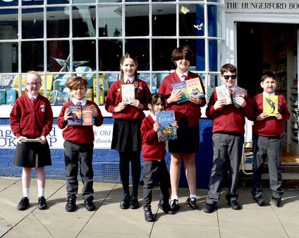A row of primary pupils are standing in front of a bookshop holding their books and smiling.