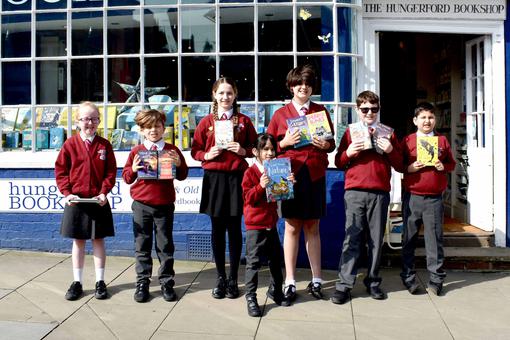 A row of primary pupils are standing in front of a bookshop holding their books and smiling.