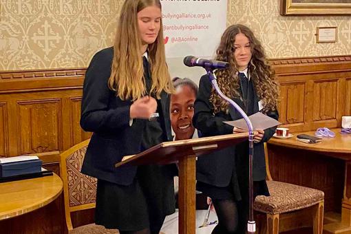 Two young female students are standing and speaking at a podium.
