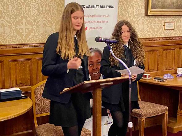 Two young female students are standing and speaking at a podium.