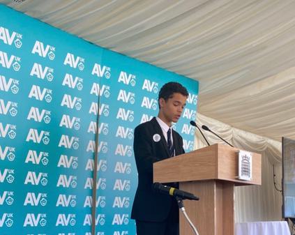 A pupil is making a speech standing at a lectern on a stage.
