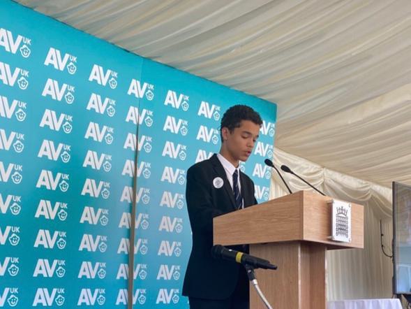 A pupil is making a speech standing at a lectern on a stage.