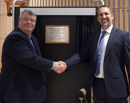 Two men are shaking hands and standing in front of a plaque