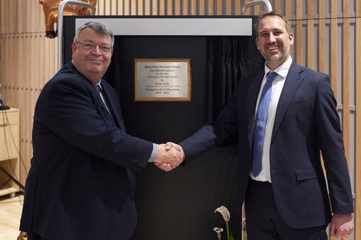 Two men are shaking hands and standing in front of a plaque