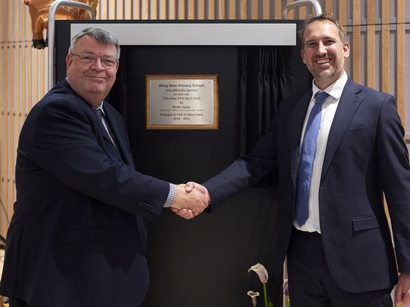 Two men are shaking hands and standing in front of a plaque