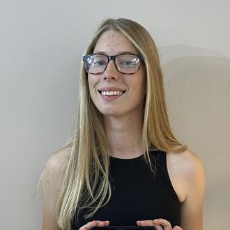 A young adult female is smiling whilst presenting her phone with results