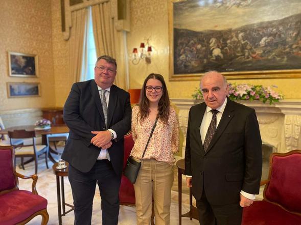 Three people are stood in a line in a grand room.