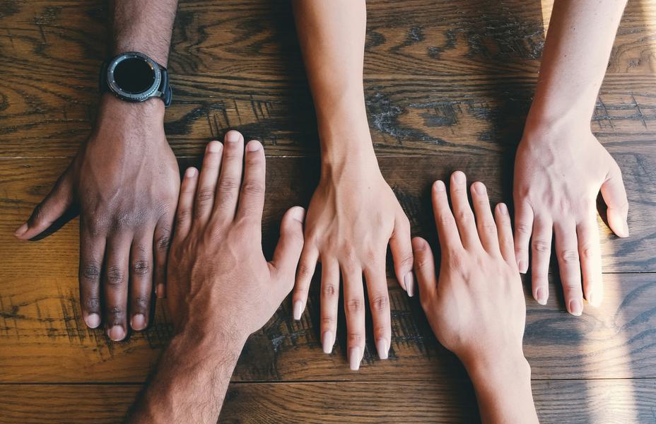 Five hands placed down on a brown surface