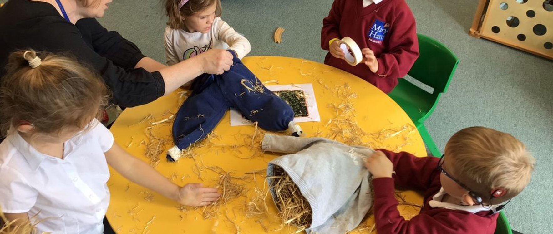 Children are sitting at a table and making a guy for guy fawkes day
